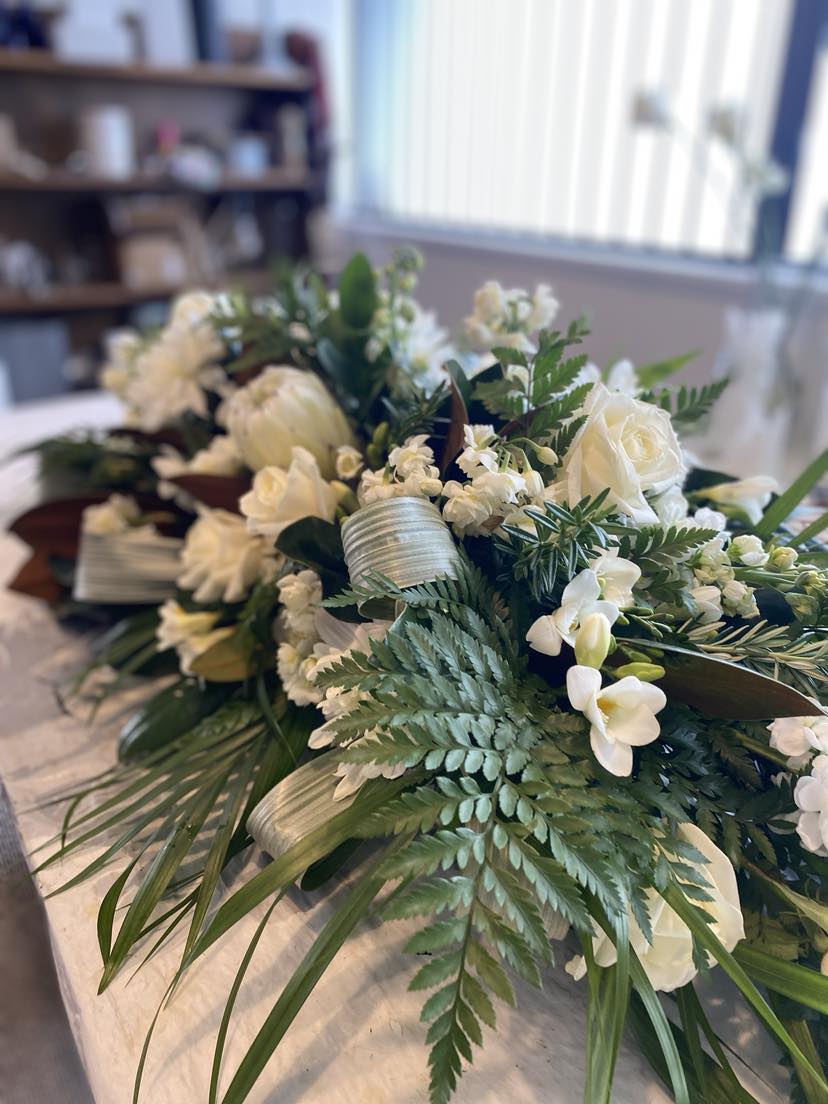 Traditional shaped casket spray in greens & whites with interesting textures & blooms