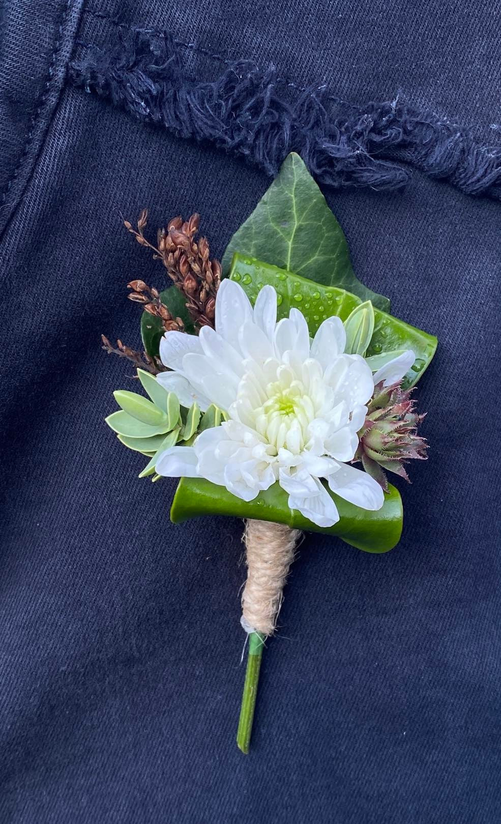 A Buttonhole with a single flower and interesting foliage with ribbon around the stems