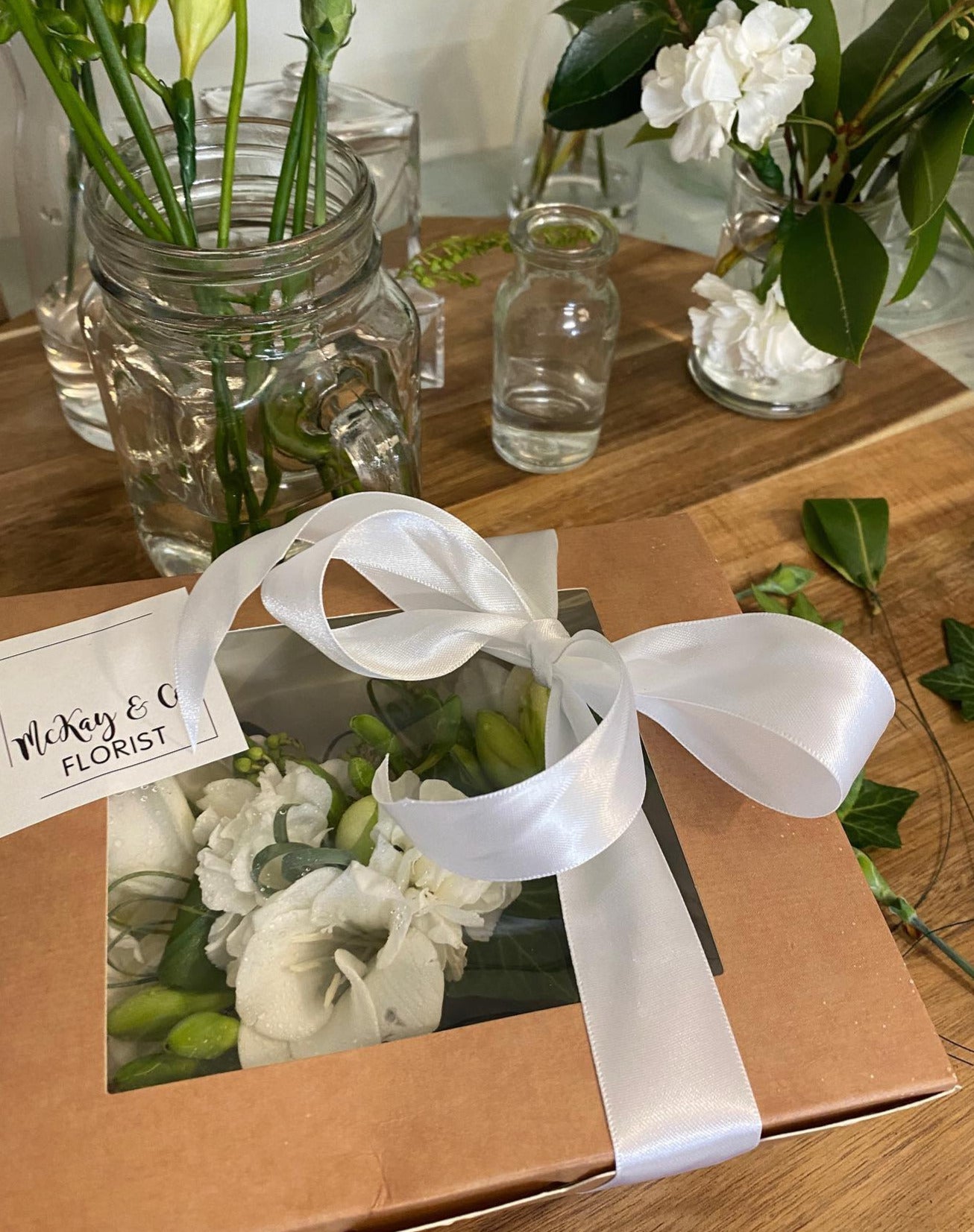 A gorgeous wrist corsage made with white flowers and interesting green foliage to complement any outfit. With a matching buttonhole to complete the look. Included is a box of locally hand crafted Adelphi Chocolates.