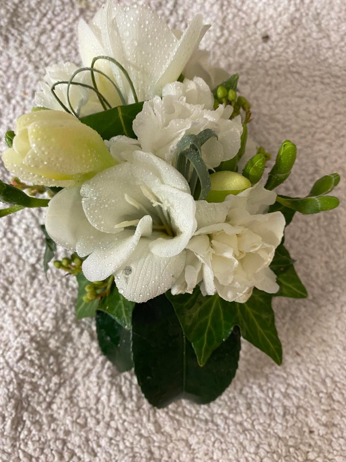 A gorgeous wrist corsage made with white flowers and interesting green foliage to complement any outfit.